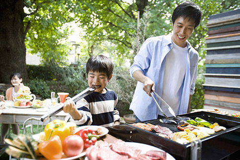 A father and son preparing food in an outdoor kitchen using a gas BBQ grill.