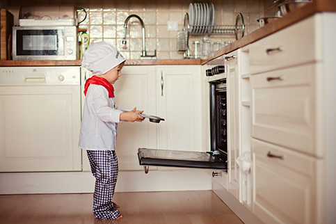 A child standing in a kitchen next to a modern gas oven to bake