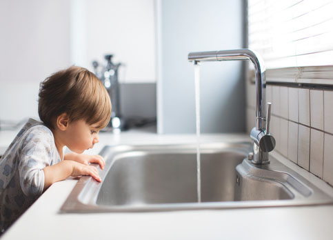 Child drinking clean water from a kitchen tap connected to a reliable gas water heating system.