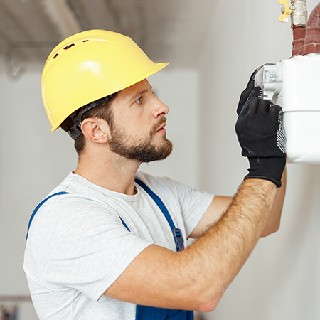 Electrician in a yellow hard hat installing or repairing a gas heating or electrical system.
