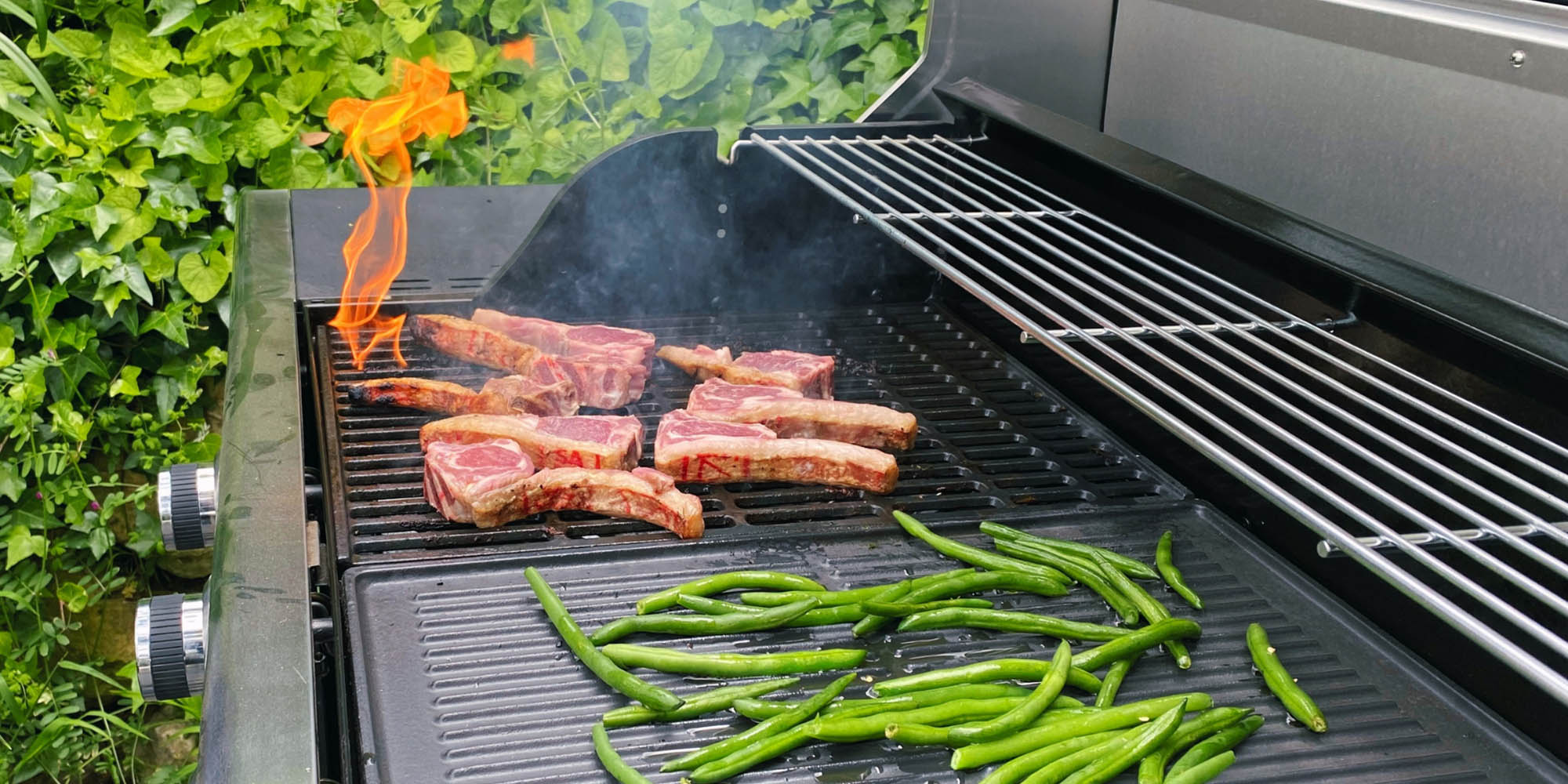Close-up of steaks and vegetables being grilled on a gas BBQ.
